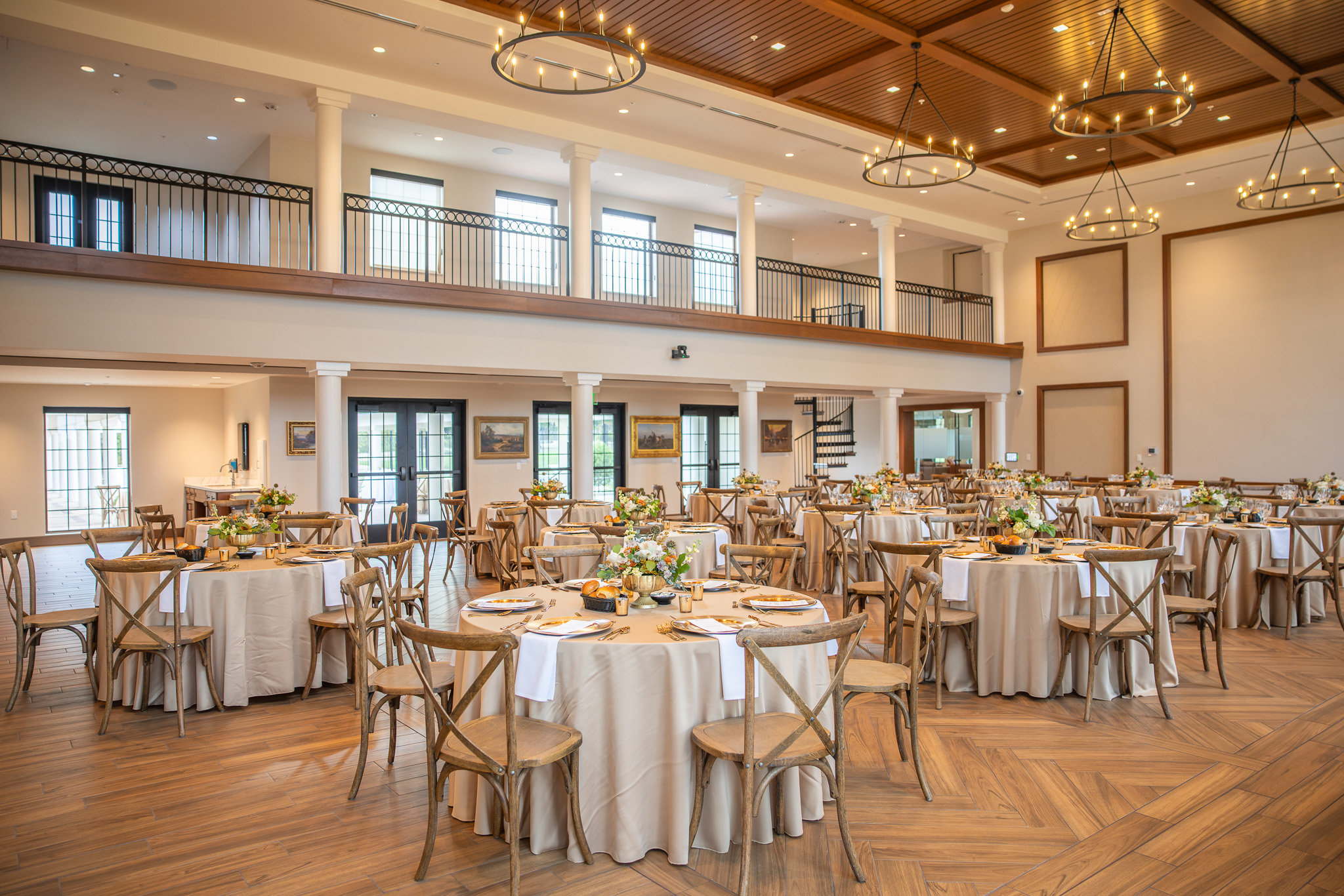 Elegant event space featuring round tables with beige tablecloths, ready for a gathering. Large windows and decorative lighting enhance the ambiance.