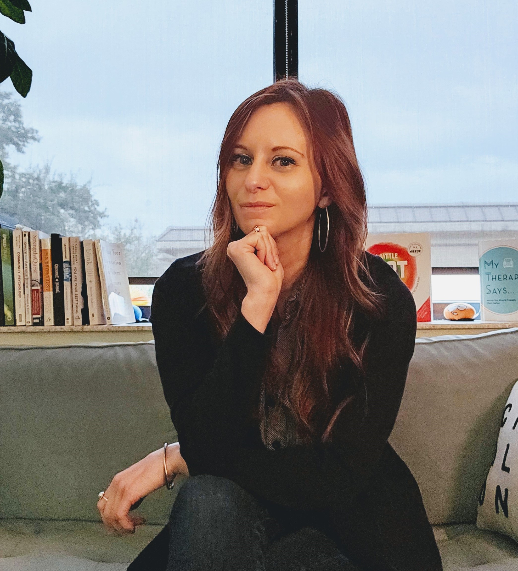 Katie sitting on a couch in her office with chin resting on her hand and elbow on her knee