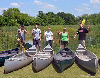 5 individuals standing next to boats with  paddles