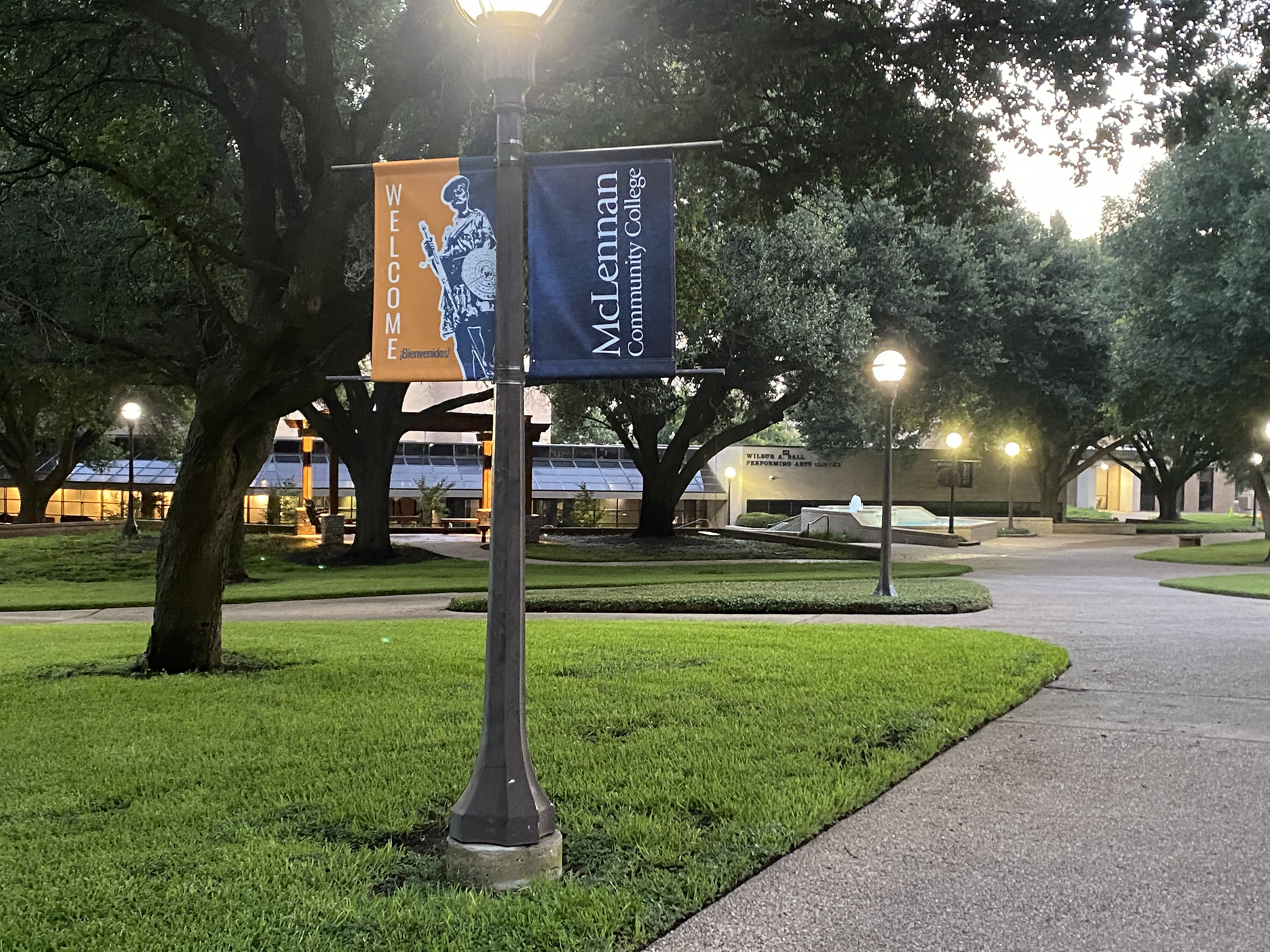 Welcome banner for McLennan Community College, featuring a welcoming figure and set in a landscaped outdoor area with trees and lighting.