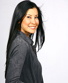 A smiling woman with long black hair poses confidently in a gray jacket.