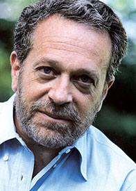 Portrait of Robert Reich, an economist and former Secretary of Labor, featuring his characteristic beard and blue shirt.