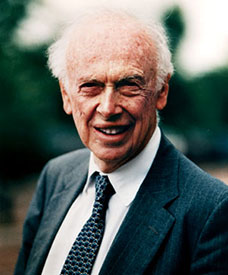 Portrait of James Watson, co-discoverer of the DNA structure, smiling in a suit and tie.