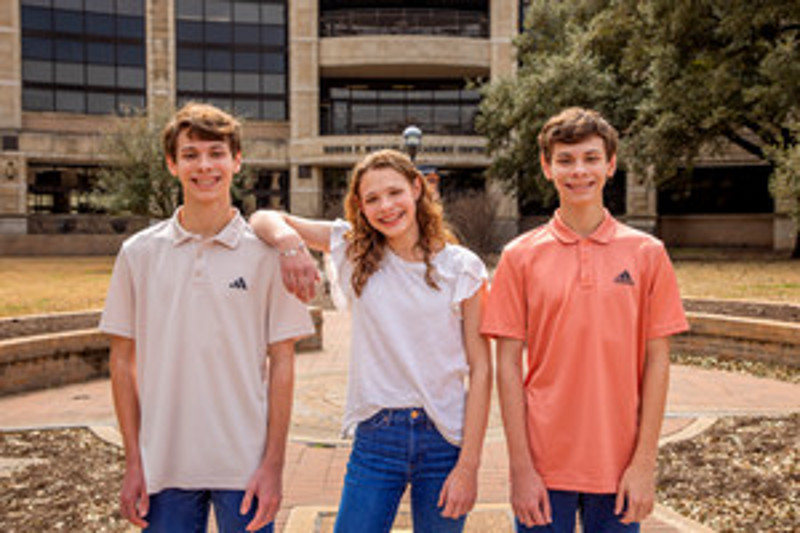 Three teenagers wearing branded polo shirts pose together outdoors in front of a modern building.