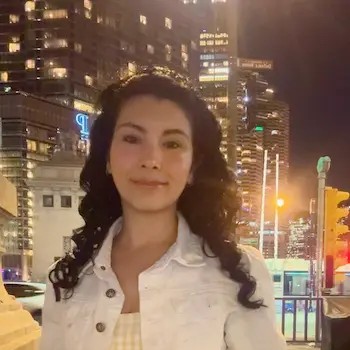 Person smiling outdoors at night with illuminated city skyscrapers in the background.