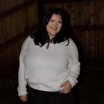 Person in a white sweater smiling while standing inside a wooden barn.