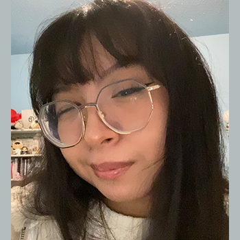 Close-up selfie of a person with long dark hair and large round glasses, winking at the camera.