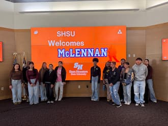 Group of students posing in front of a large SHSU screen that reads “SHSU Welcomes McLennan” at Sam Houston State University.